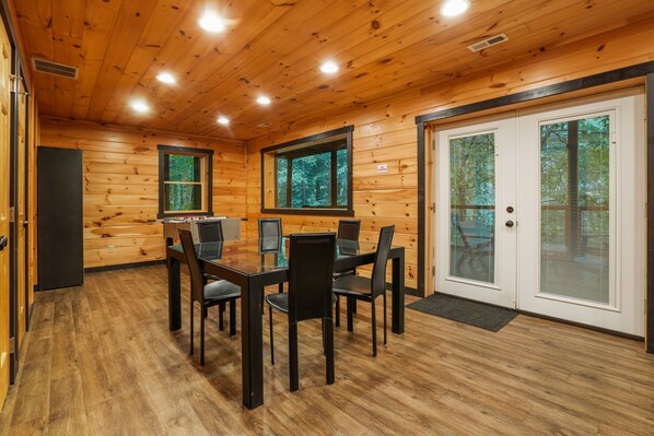 A wooden-paneled room with a glass-top dining table and chairs, a door with a window, and a door with a window.