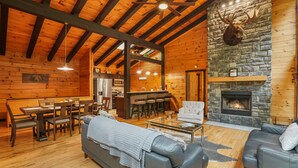 A log cabin interior with a stone fireplace, wooden beams, a dining area, and a cozy seating arrangement. - Outside Inn | Hocking Hills, Hot Tub, Views (Sugar Grove)