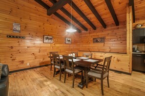 A wooden cabin interior with a dining table, chairs, and a kitchen area.