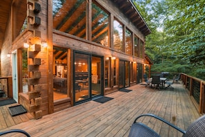 A wooden cabin with a deck, large windows, and a dining area.