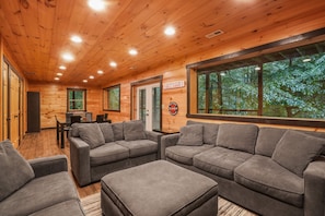 A wooden interior with a large window, grey sofas, and a basketball court sign.