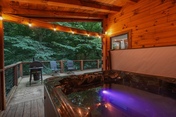 A wooden deck with a hot tub, a barbecue grill, and two chairs.