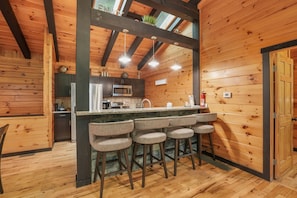 A wooden interior with a kitchen area featuring a bar stool setup, a microwave, and a sink.