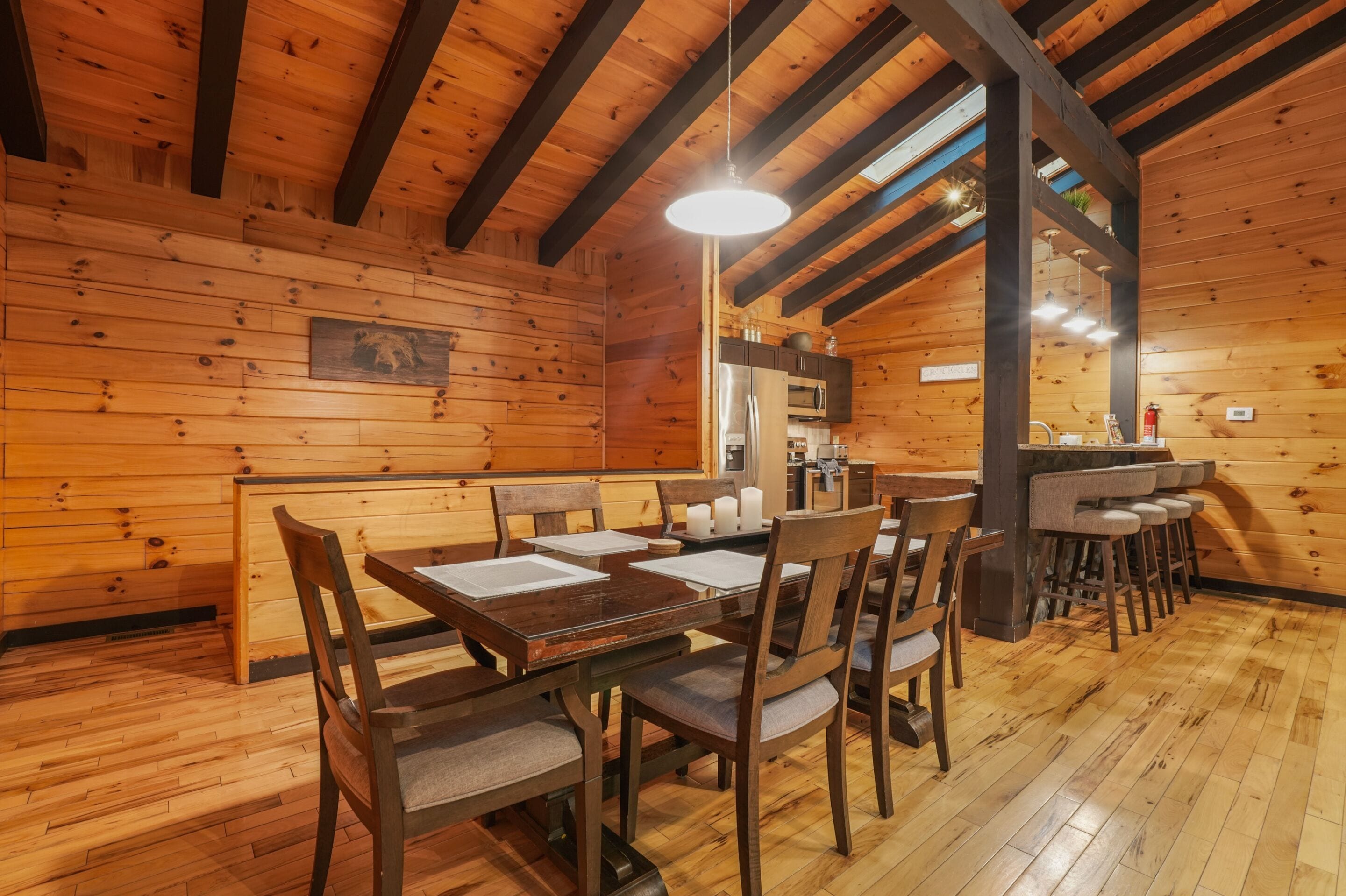 A wooden interior with a dining area featuring a table and chairs, a kitchen area with appliances, and a bar with stools.