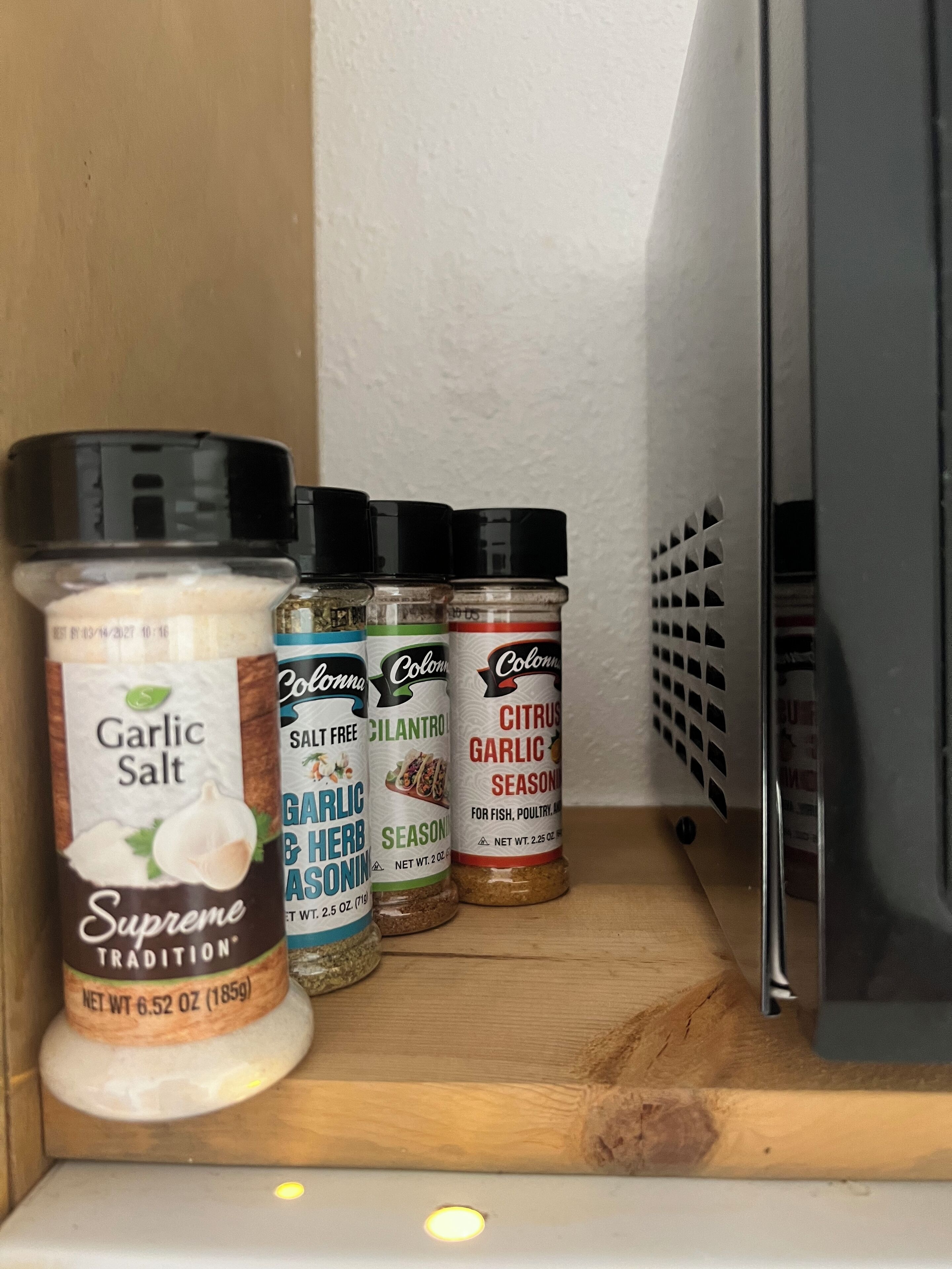 A shelf with four spice containers labeled Garlic Salt, Garlic Herb Seasoning, Salt-Free Cilantro Seasoning, and Citrus Garlic Seasoning.
