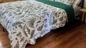 Ein Schlafzimmer mit Bett, Holzboden, einer grünen Tagesdecke und einem Bild an der Wand.