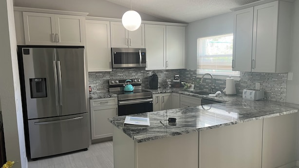 A modern kitchen with stainless steel appliances, white cabinets, a granite countertop, and a hanging light fixture.