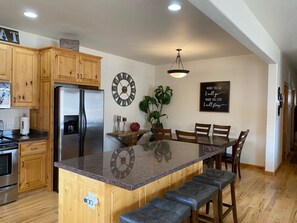A kitchen with wooden cabinets, a stainless steel refrigerator, a marble island with bar stools, a clock, and a motivational quote on the wall. - 3-bedroom beautiful house in downtown Moab with AC, WiFi, amazing location. (Moab)