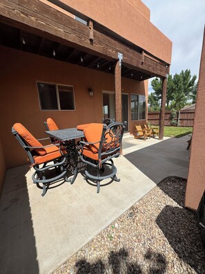 An outdoor patio with a table and chairs, a covered area, and a view of a backyard.