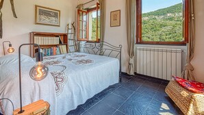Ein Schlafzimmer mit Bett, Bücherregal, Fenster mit Blick und Heizkörper.