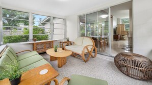 Ein moderner, offener Wohnbereich mit Balkon, ausgestattet mit Rattanmöbeln, einem runden Holztisch und einem grünen Sofa.