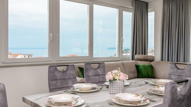 A dining area with a table set for four, large windows, and a view of the sea. - Amazing apartment in Podstrana with WiFi (Podstrana)