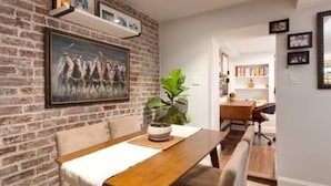 A dining area with a brick wall, a painting, and a potted plant.