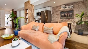 A modern living room with a sofa, a coffee table, and a dining area with a brick wall and a painting.