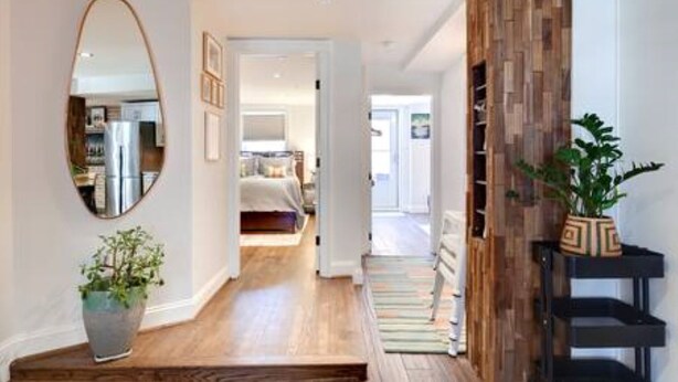 A hallway with a wooden floor, a mirror, a potted plant, and a black shelf unit.