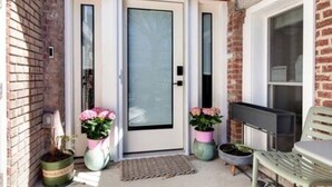 A brick exterior with a white door, two potted plants, a bench, and a small table.