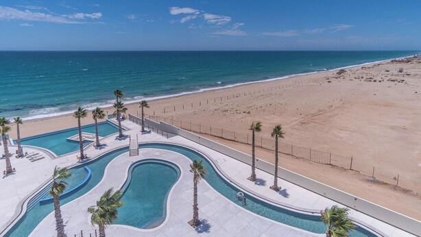 Un complejo turístico con piscina, palmeras y playa.
