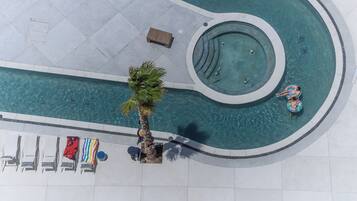 Eine Vogelperspektive auf einen Swimmingpool mit einer runden Whirlwanne, Liegestühlen und einer Palme.