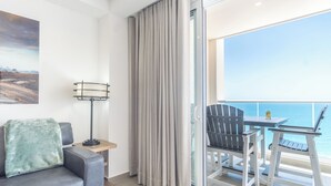 Un balcón con mesa y sillas, un sofá, una lámpara de pie y vistas al mar.