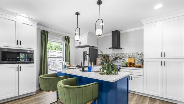 Una cocina moderna con armarios blancos, una isla azul, taburetes verdes y luces colgantes.