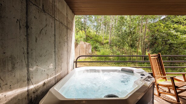 Un bain à remous avec une terrasse en bois et une chaise, donnant sur une zone boisée.