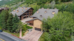 Un grand chalet à étages, avec une façade en pierre et en bois, plusieurs cheminées et une allée menant à un garage.
