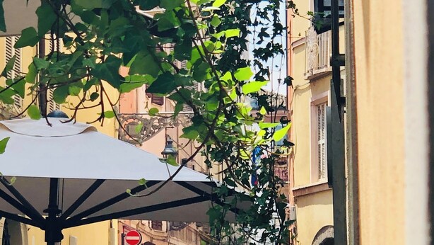 An outdoor café area with tables and chairs, surrounded by greenery and buildings. - Apartment Battistero XX Marzo (Parma)
