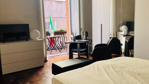 A hotel room with a bed, a desk with a chair, a television, and a small table with a plant. - Apartment Battistero XX Marzo (Parma)