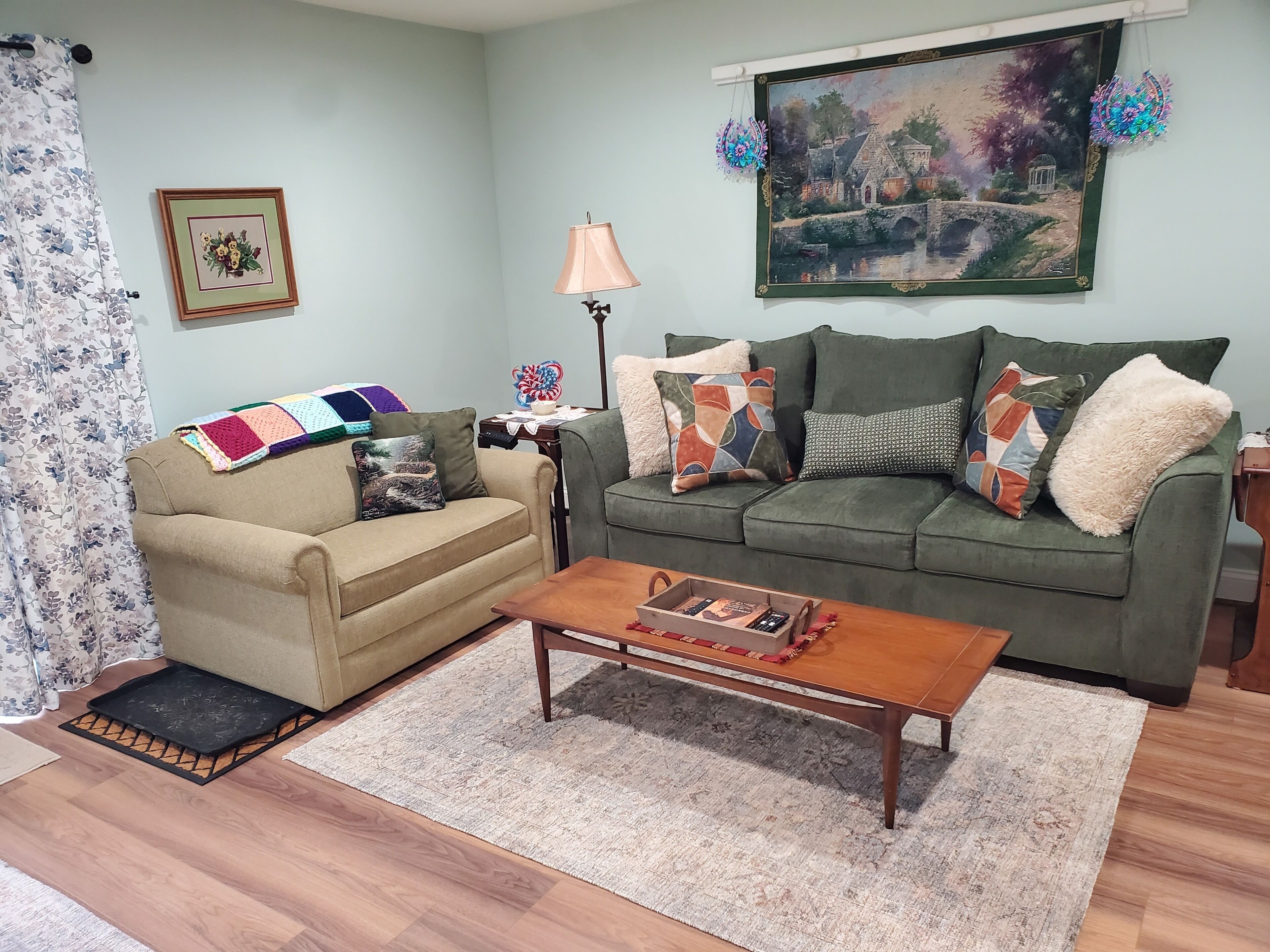 Sala de estar com dois sofás, uma mesa de centro, uma luminária, um quadro e uma cortina florida.
