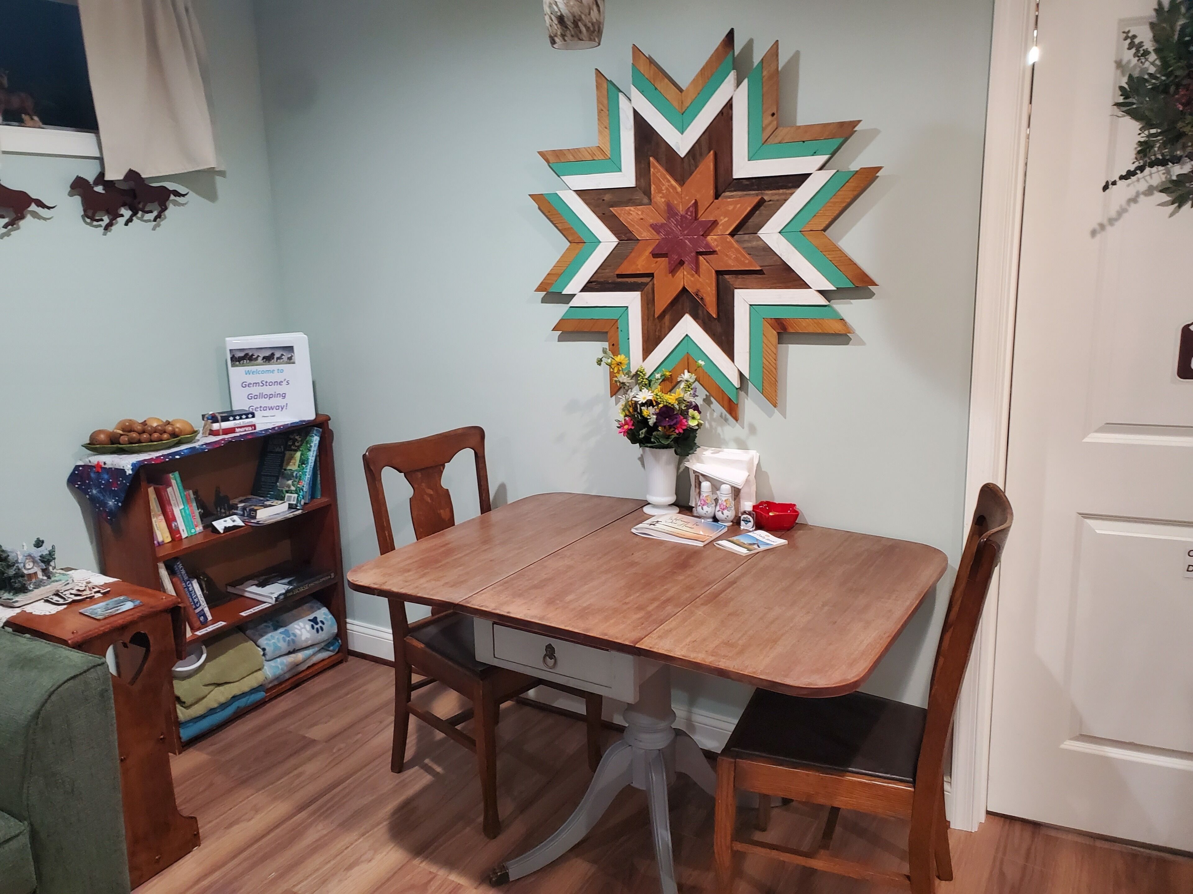 Un comedor con una mesa de madera, sillas, una estantería y un adorno en la pared.