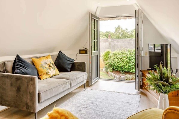 A modern living room with a grey sofa, a flat-screen TV, and a sliding glass door leading to a garden.