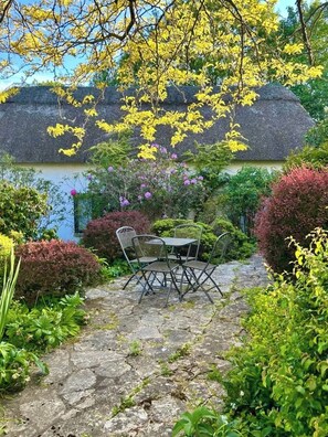 A stone pathway leading to a thatched-roof building with a table and chairs in the center.