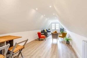 A modern loft apartment with a dining area, a living space with a sofa and chairs, and a view through a large window.