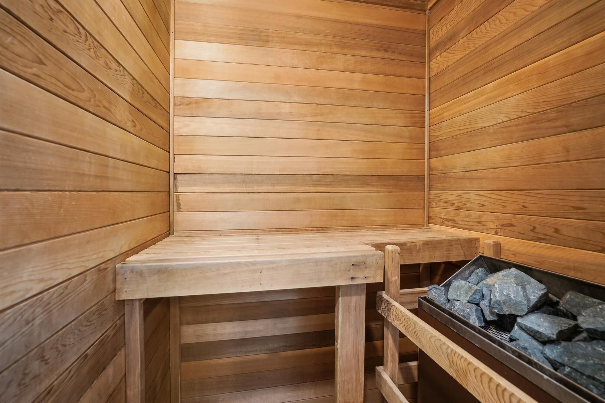 A wooden sauna with a bench and a stone-filled container.