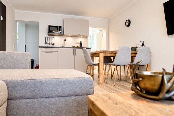 Una cocina moderna con microondas, armarios y una zona de comedor con mesa y sillas de madera.