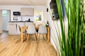Una cocina moderna con una mesa y sillas de madera, un microondas y una botella de vino sobre la encimera.
