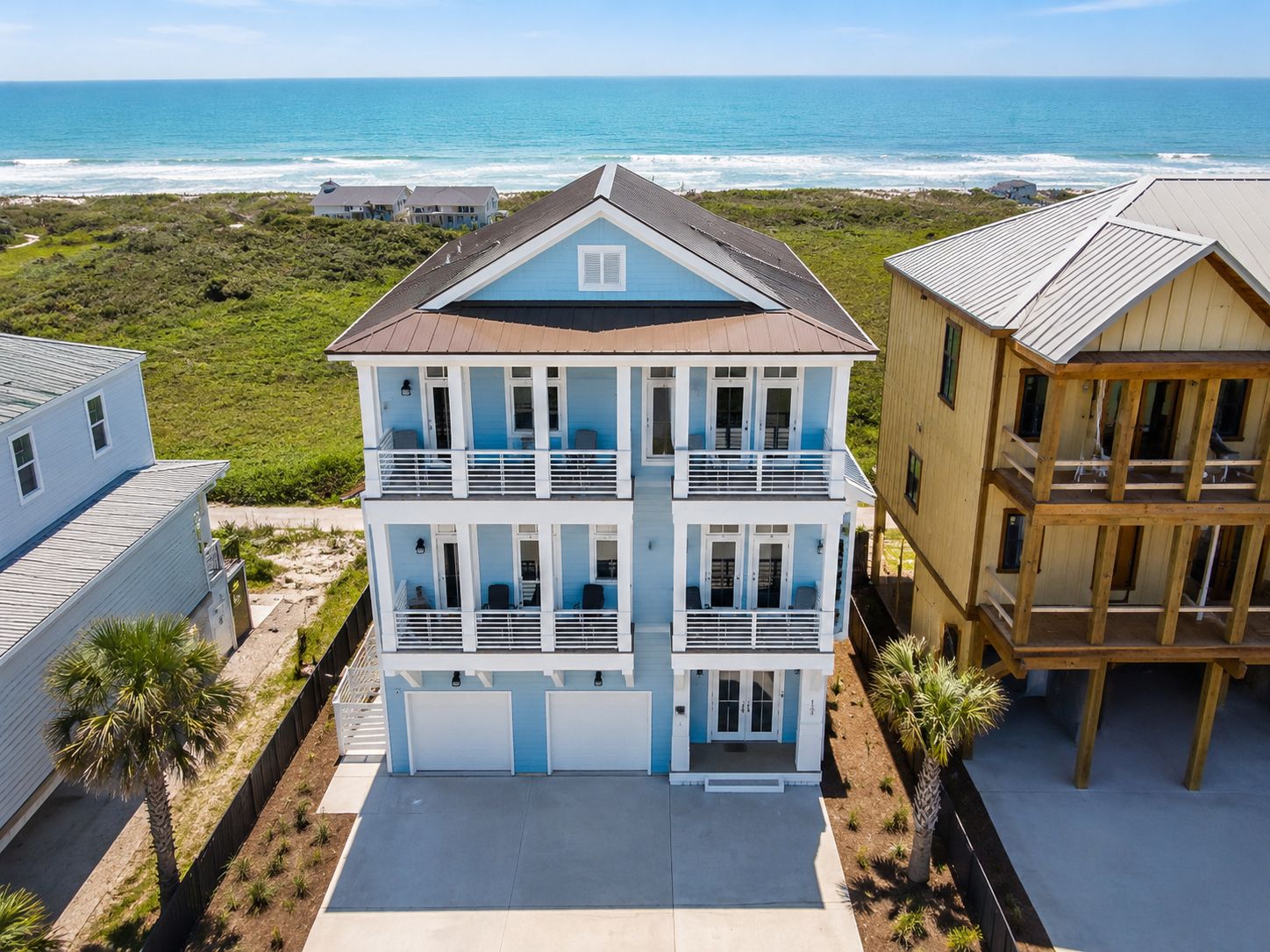 Una casa fronte spiaggia su due piani, con un balcone, un garage e vista sull'oceano.