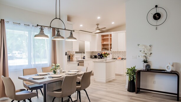 Een moderne keuken met witte kasten, een eethoek met een tafel en stoelen, en een klok aan de muur.