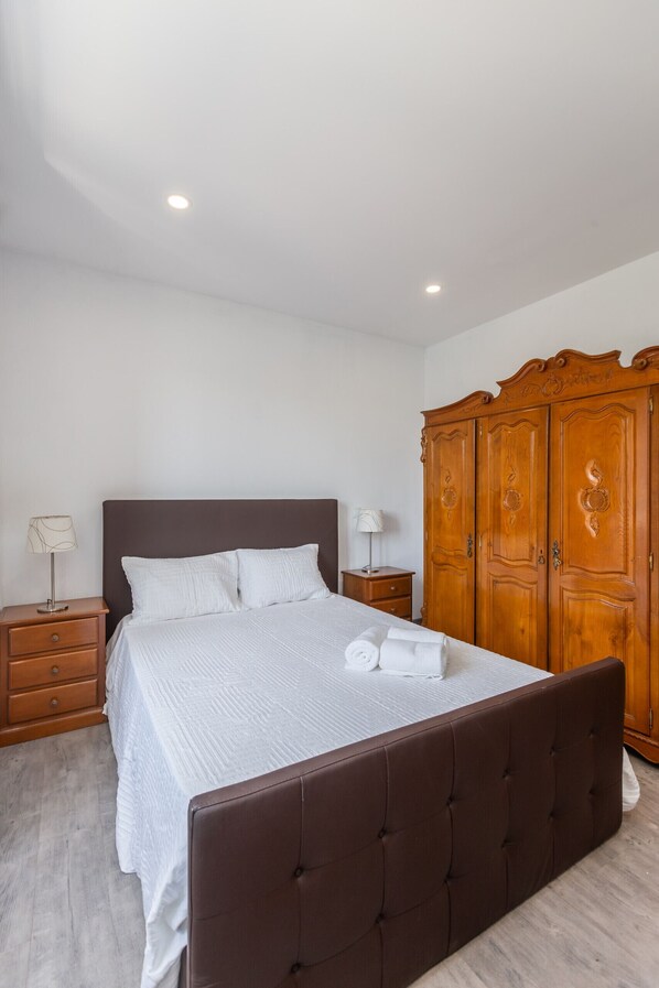 Une chambre à coucher avec un grand lit, une armoire en bois, deux tables de chevet avec des lampes et une palette de couleurs neutres.