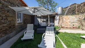 En patio med to hvide liggestole, et bord og en stor parasol.