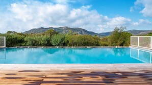 A swimming pool with a wooden deck, surrounded by greenery and mountains in the background.