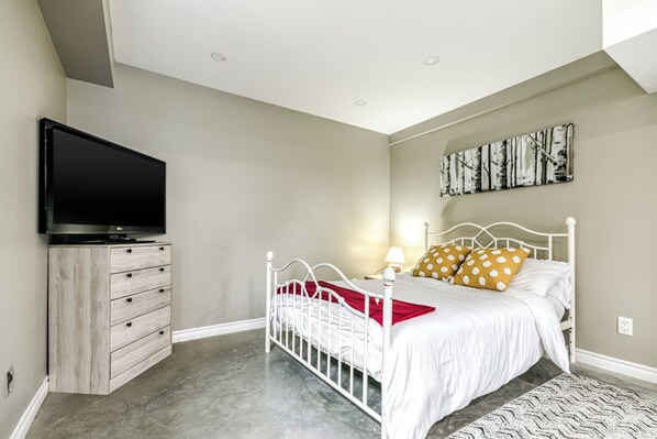 A bedroom with a bed, a dresser, a television, and a wall-mounted artwork. - Cozy Comfy Studio (Greater Sudbury)