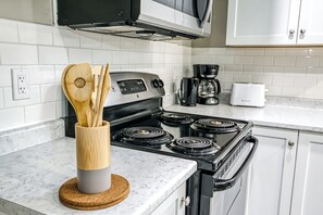 A kitchen with a stove, microwave, and coffee maker. - Cozy Comfy Studio (Greater Sudbury)