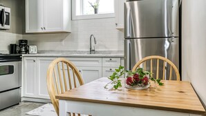 Een moderne keuken met witte kasten, een roestvrijstalen koelkast, een houten eettafel en twee houten stoelen.