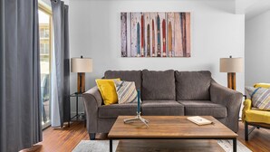 A living room with a grey sofa, a wooden coffee table, and a colorful abstract painting on the wall. - Fun Ski Condo - On Ski Bus Line - Pool & Hot Tub (Steamboat Springs)
