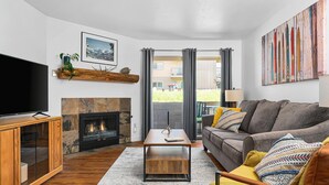 A modern living room with a fireplace, a sofa, a coffee table, and a television. - Fun Ski Condo - On Ski Bus Line - Pool & Hot Tub (Steamboat Springs)
