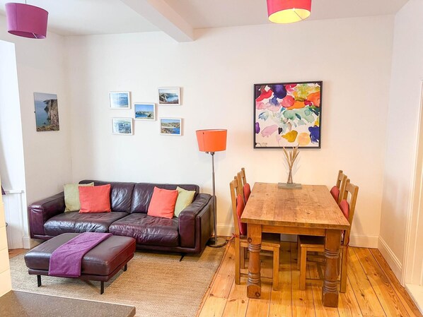Una sala de estar con un sofá de cuero, una mesa de comedor de madera y un cuadro abstracto de colores.