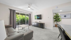 Una sala de estar moderna con un sofá, una mesa de comedor, un televisor y un ventilador de techo.