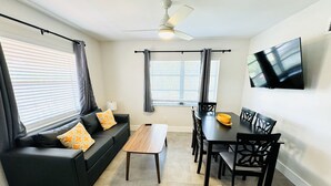 Una sala de estar moderna con un sofá negro, una mesa de centro de madera y una mesa de comedor con sillas.