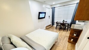 Habitación de hotel con cama, escritorio, silla, televisor y ventana con persianas.